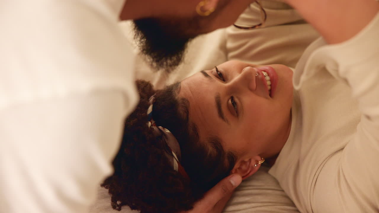 pareja acurrucada en la cama, sonriendo y besándose