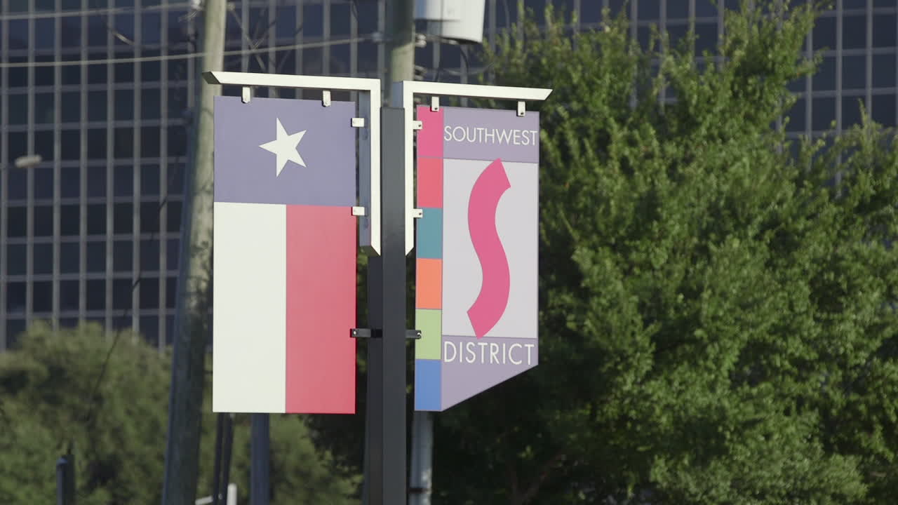 un letrero del distrito suroeste junto a una bandera de texas colgado de un poste de luz en houston