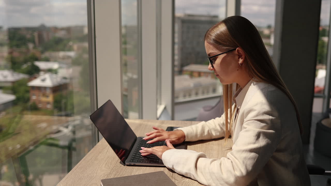 Bella giovane donna con gli occhiali seduta a un tavolo in ufficio e che lavora al laptop. Una donna d'affari parla al telefono al lavoro.