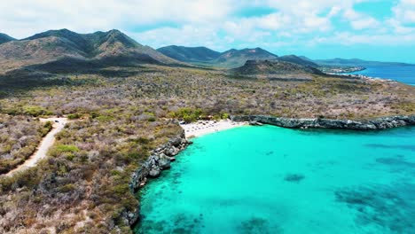 el dron está volando sobre el océano mirando a una pequeña playa y las montañas en el fondo en curacao imágenes aéreas 4k