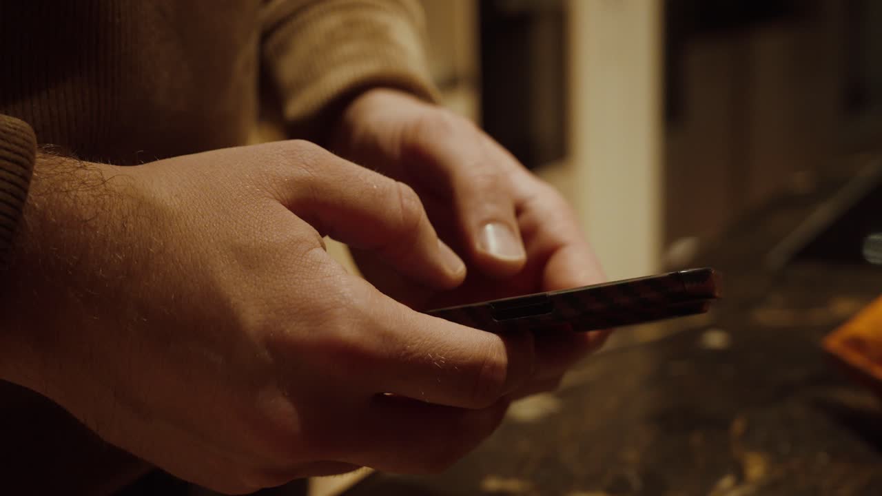 Primo piano di mani che utilizzano uno smartphone su un bancone della cucina. Concetto di uso quotidiano della tecnologia, comunicazione digitale, stile di vita moderno e routine domestica.