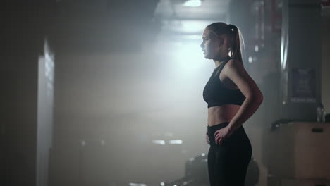 Mujer-Joven-Descansando-Después-De-Su-Entrenamiento-Y-Mirando-Hacia-Abajo.-Atleta-Femenina-Descansando-Después-Del-Entrenamiento-Físico-En-El-Gimnasio-Oscuro