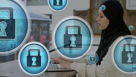 animation of padlock icons over biracial woman wearing hijab working on laptop in cafes