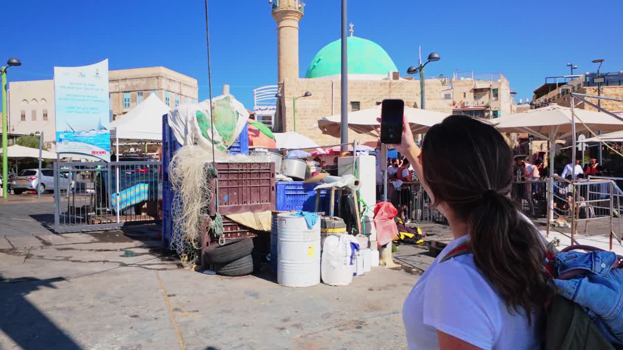 Donna turista che scatta una foto a una moschea con cupola verde usando lo smartphone.