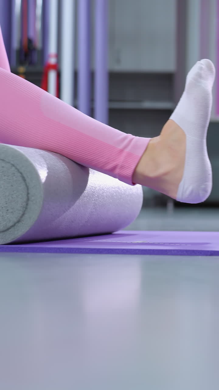 vista de las piernas de dos personas que participan en una sesión de fitness en esteras de yoga usando rodillos de espuma para ejercicios de piernas en un gimnasio bien iluminado, centrándose en el estiramiento y la recuperación muscular