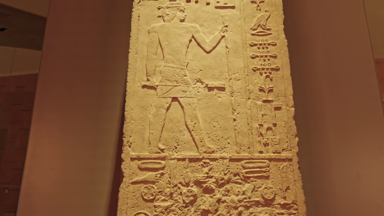 Limestone relief featuring a single standing male figure with hieroglyphic text, most likely a fragment of a funerary stela or a section from a tomb wall in the Grand Egyptian Museum (GEM)