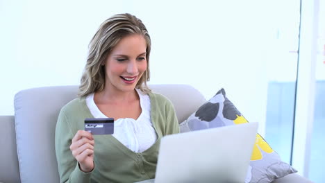 mujer encantada sosteniendo su tarjeta de crédito y usando su portátil