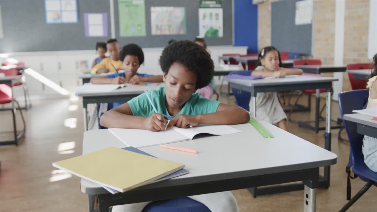 Crianças estudantes diversas e concentradas escrevendo em suas carteiras em uma sala de aula de escola primária, em câmera lenta.