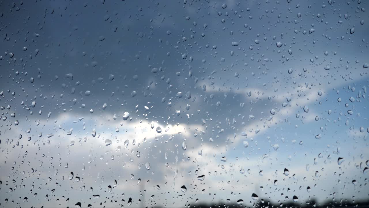 구름이 많은 하늘을 향한 비방울을 가진 차의 앞 유리창을 통한 시야. 비가 오는 날 차량의 창문 위에 물방울의 근접.