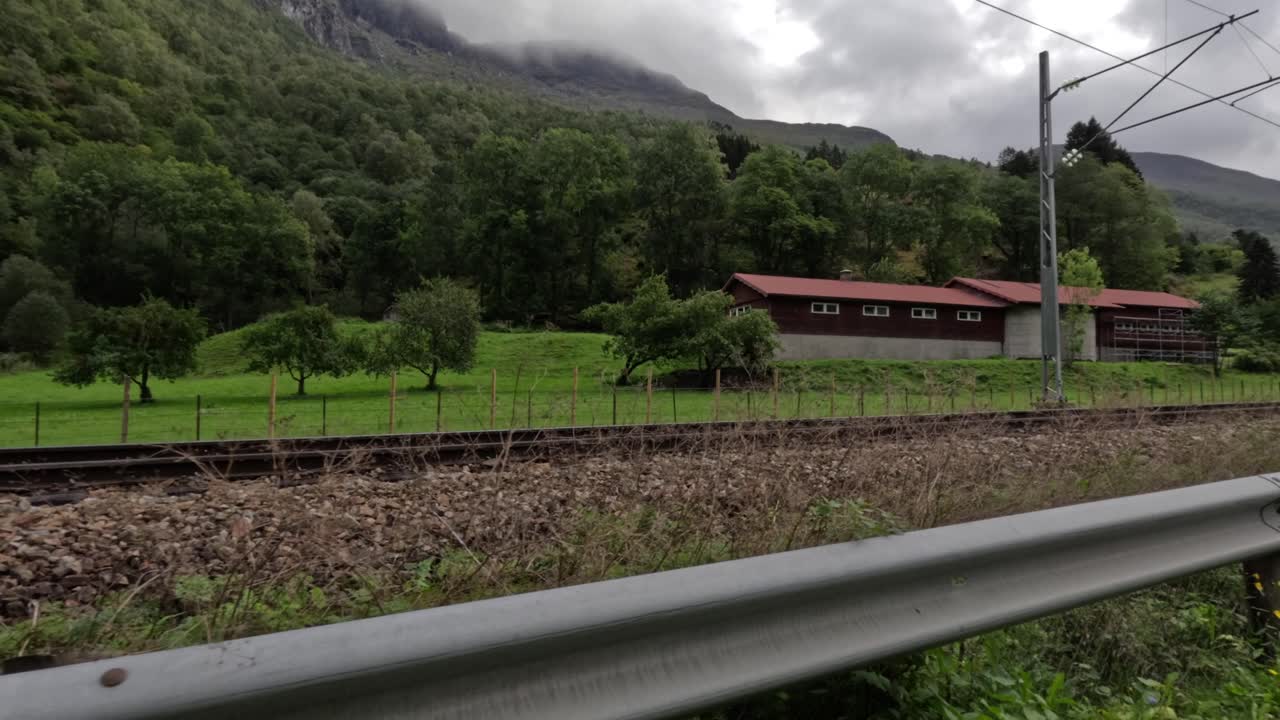 A train rolls past red-roofed buildings and misty trees as Flam’s quiet valley stretches beneath the clouds