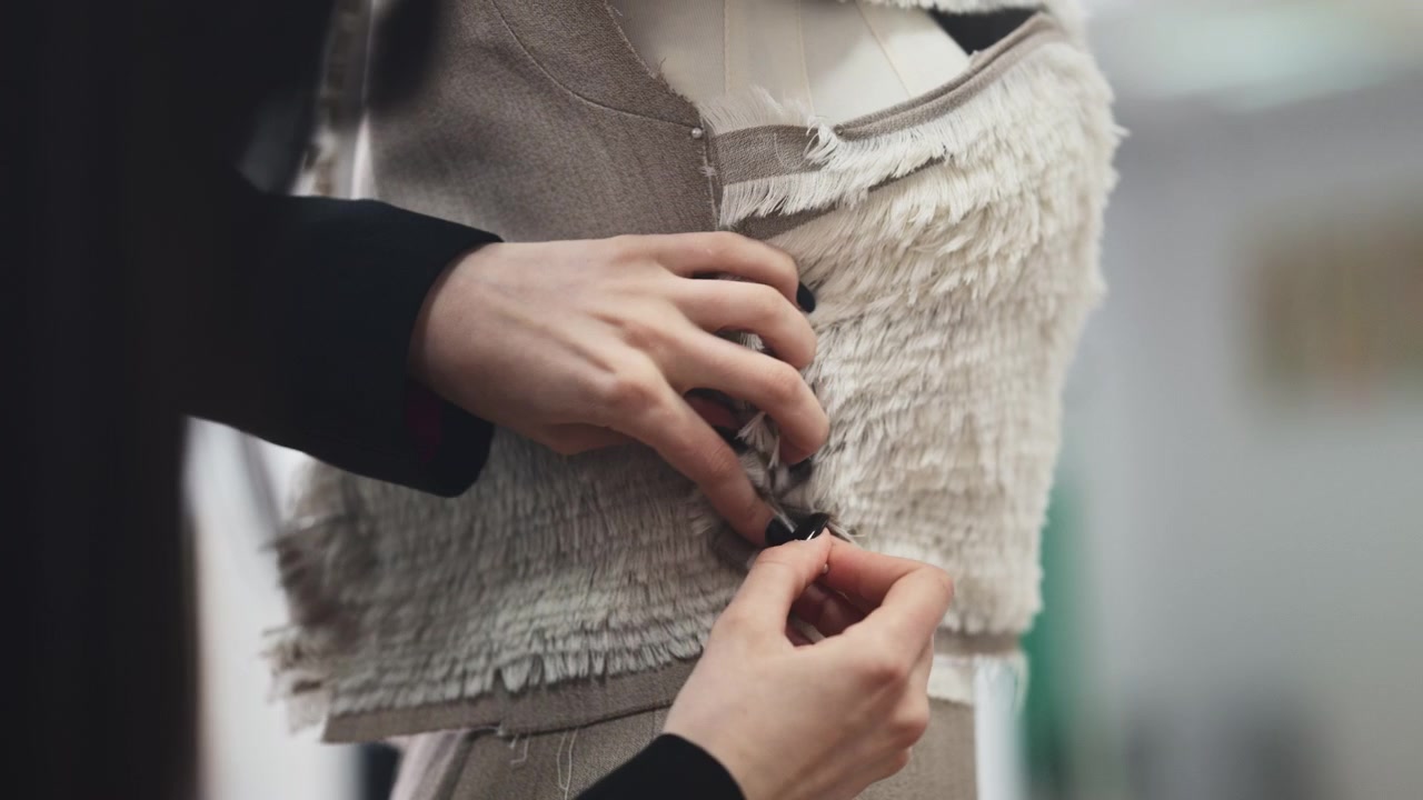 Tampilan dekat tangan yang dengan hati-hati mengangkat dan menyelaraskan sampel kain berlapis, berfokus pada tepi berumbai alami dan tekstur bahan.
