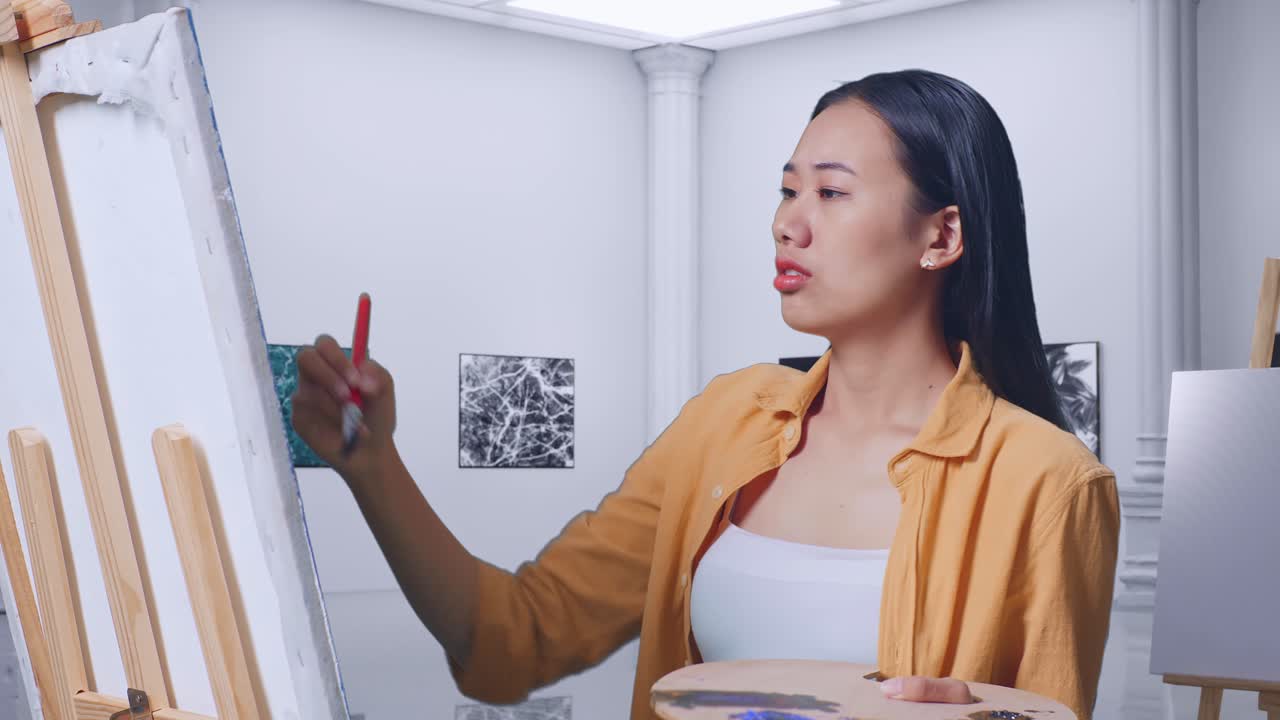 아시아 여성 예술가 가 갤러리에서 오일 페인트와 브러쉬로 그림을 그리는 동안 캔버스에 있는 그림에 불만을 품고 머리를 흔들고 있다.