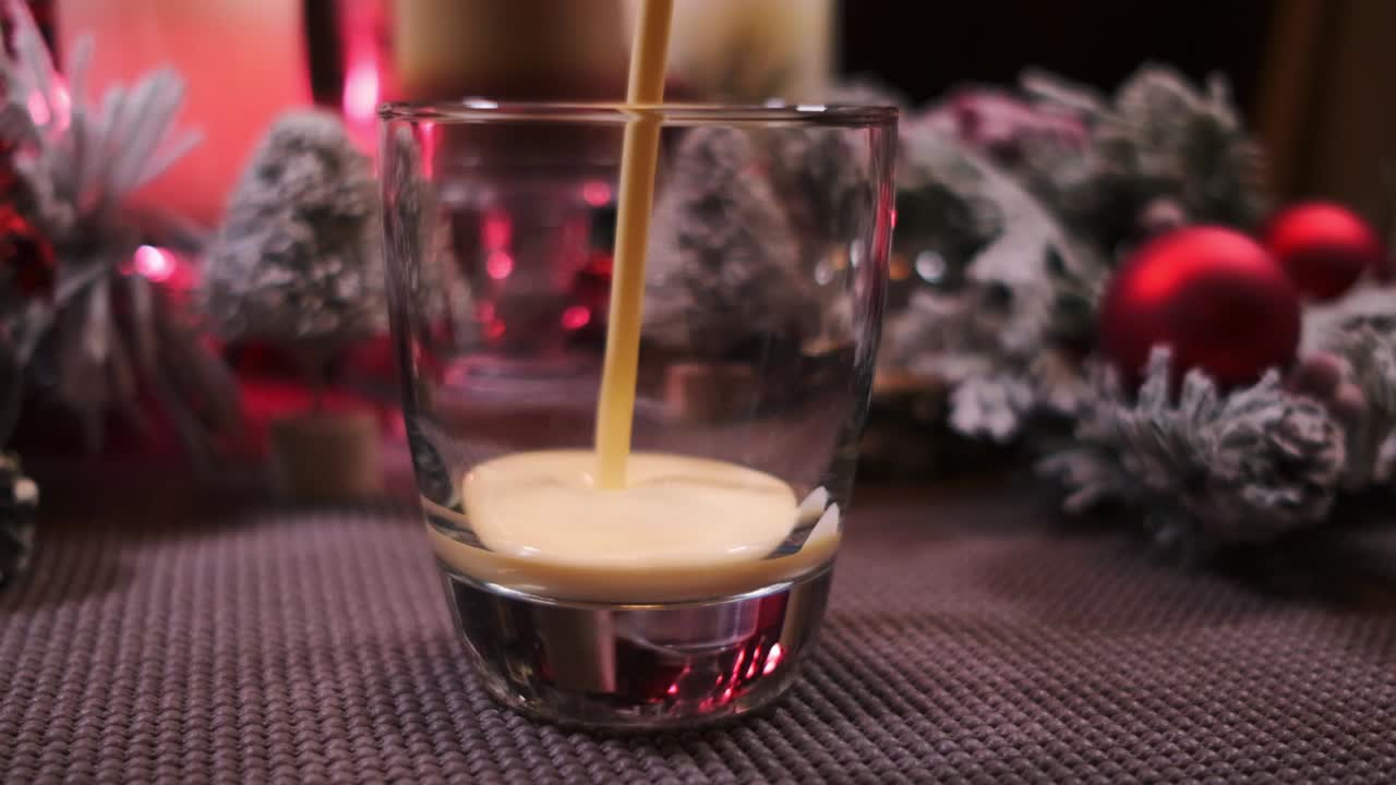 Slow motion push in of holiday drink eggnog being poured into a glass surrounded by Christmas decorations
