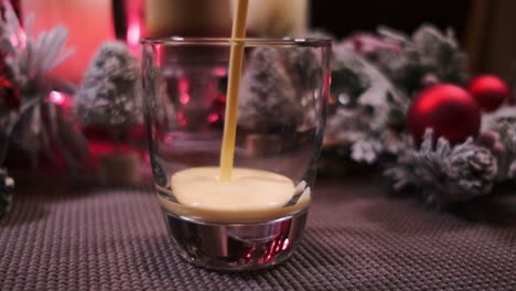 Zeitlupen-Push-In-Von-Feiertagsgetränk-Eierlikör,-Der-In-Ein-Glas-Gegossen-Wird,-Das-Von-Weihnachtsdekorationen-Umgeben-Ist