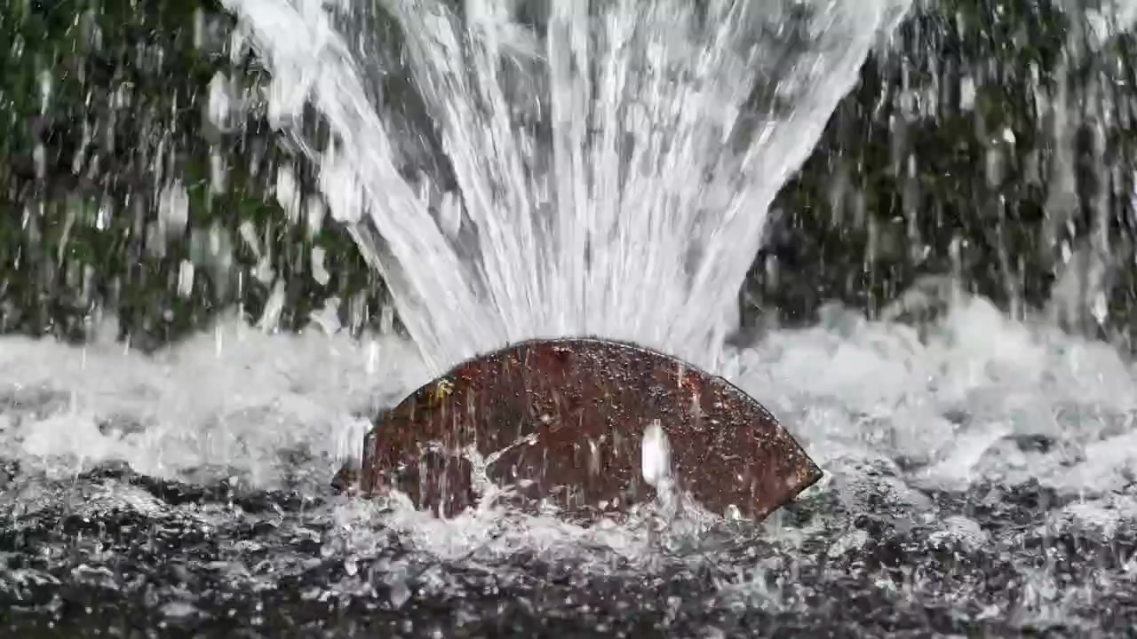 Potenti getti d'acqua zampillano verso l'alto da una bocchetta circolare di fontana marrone arrugginita.