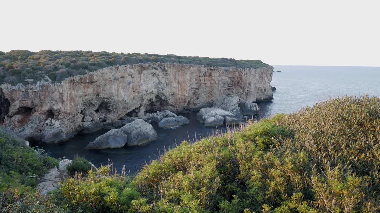 Rocky cove with rugged cliffs, green vegetation, and deep blue sea in Cala Rafalet