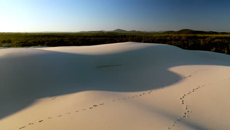 disparo de drone vuela más allá de un hombre que camina solo en dunas de arena revelando desierto