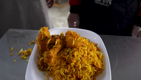 close-up of a steaming plate of chicken biryani with yellow rice and drumsticks in a local eatery. pakistan