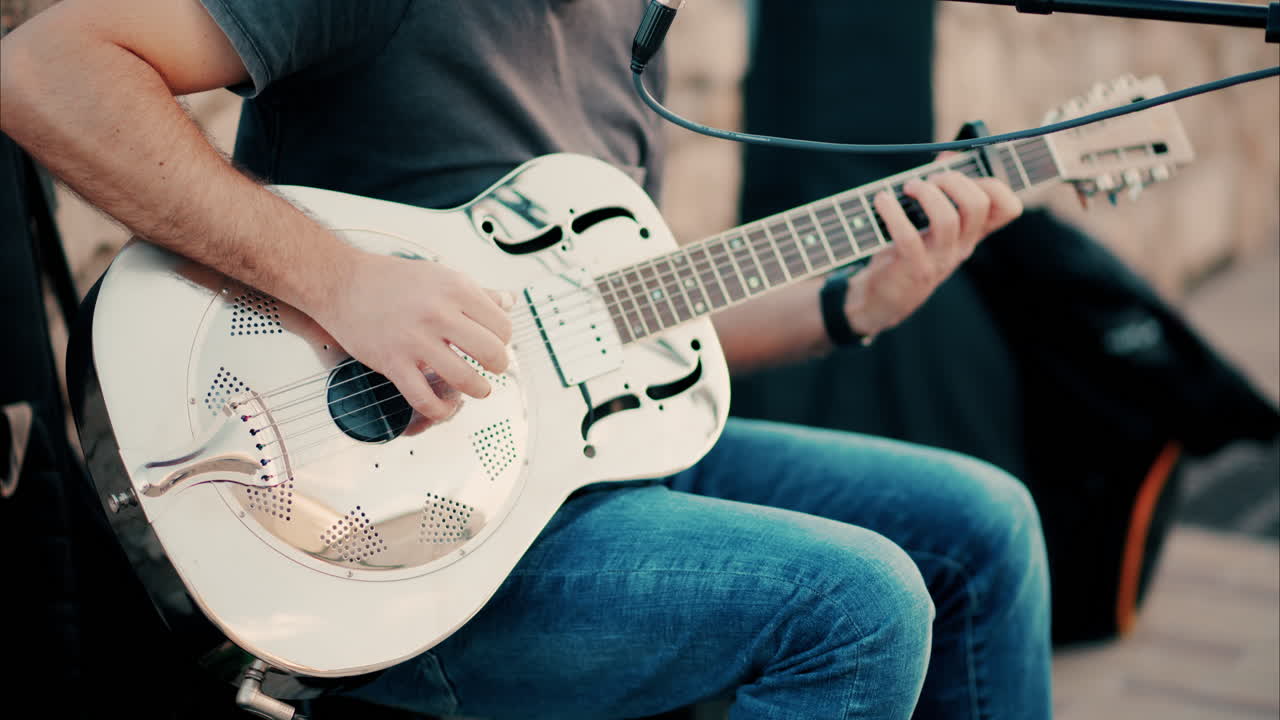 Close up of a man playing a golden esonator guitar on the street