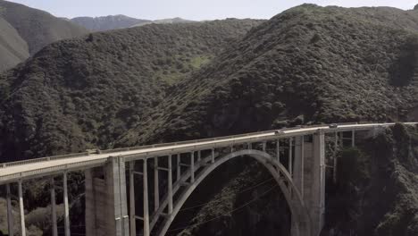 bixby creek bridge, rising aerial on a clear day, with cars traveling across, big sur