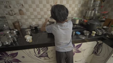 handheld shot of little asian girl boiling milk in the kitchen, from the back and side angle