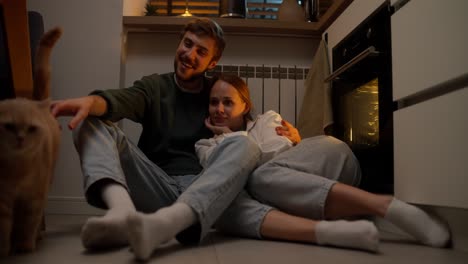 una pareja y un gato en la cocina.