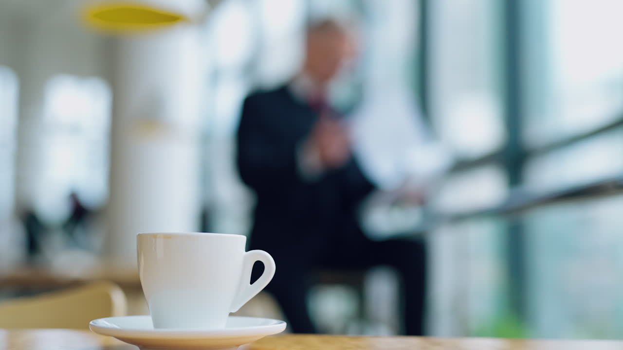 Coffee cup standing on the office desk in front view with a blurred image of businessman working on background. Morning coffe video in office.