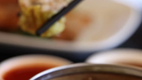 close-up of chopsticks picking up a dumpling from a bamboo steamer with sauce in the background.
