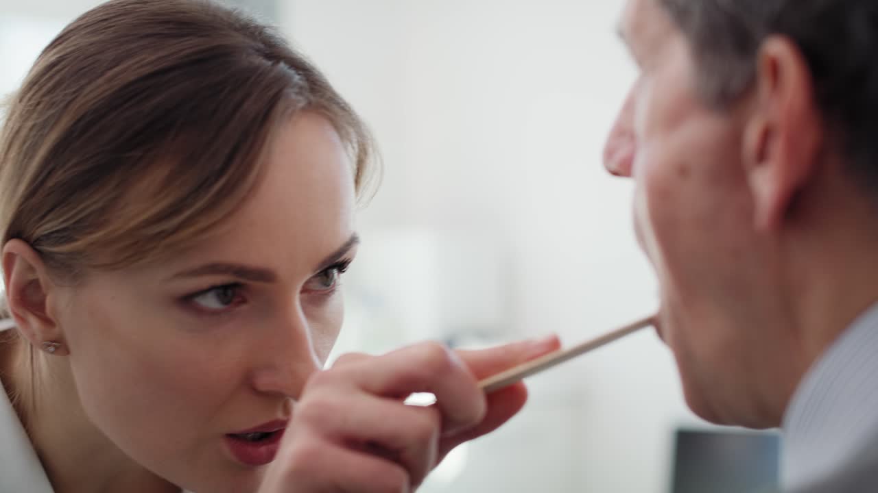 un video de mano muestra a un médico revisando la garganta de un anciano.