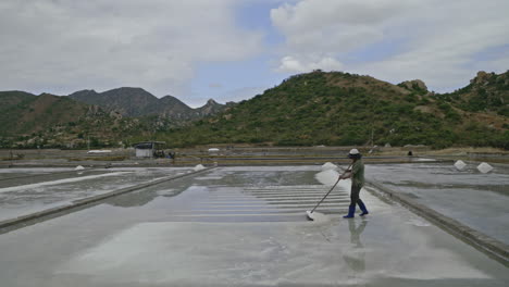 a worker raking salt in a salt field with mountains in the background