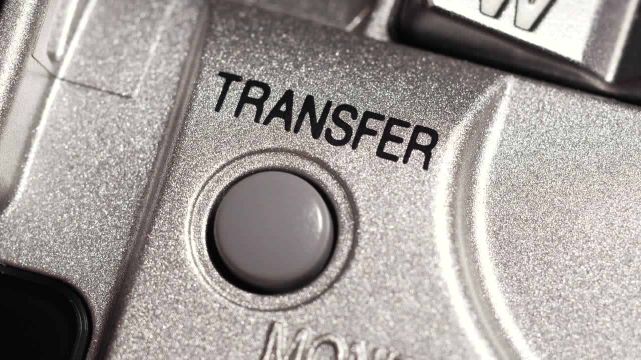 Macro close up of transfer button pressed on metallic silver panel with black lettering