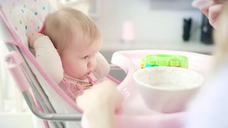 Bebé-Con-Juguete-Sentado-En-Una-Silla-Y-Comiendo-Puré.-Madre-Alimentando-Al-Bebé-Con-Cuchara