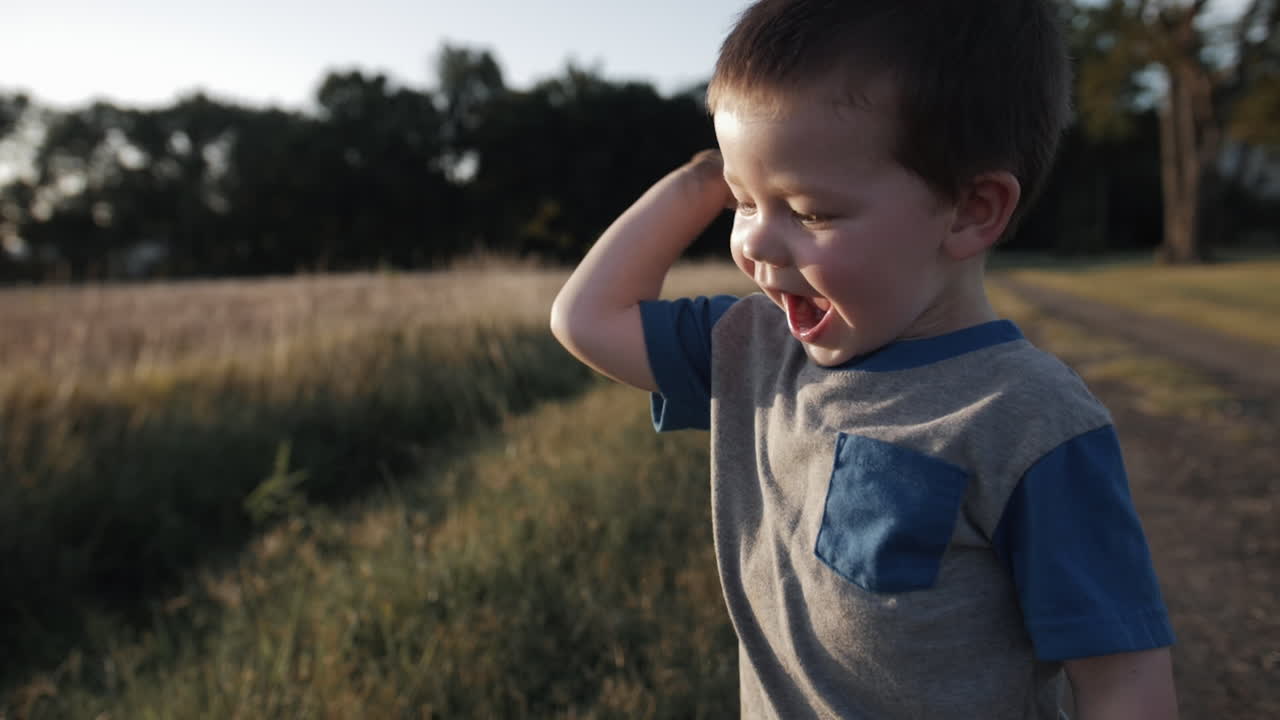 A young, happy boy playing outside and throwing dirt in sunset in cinematic slow motion