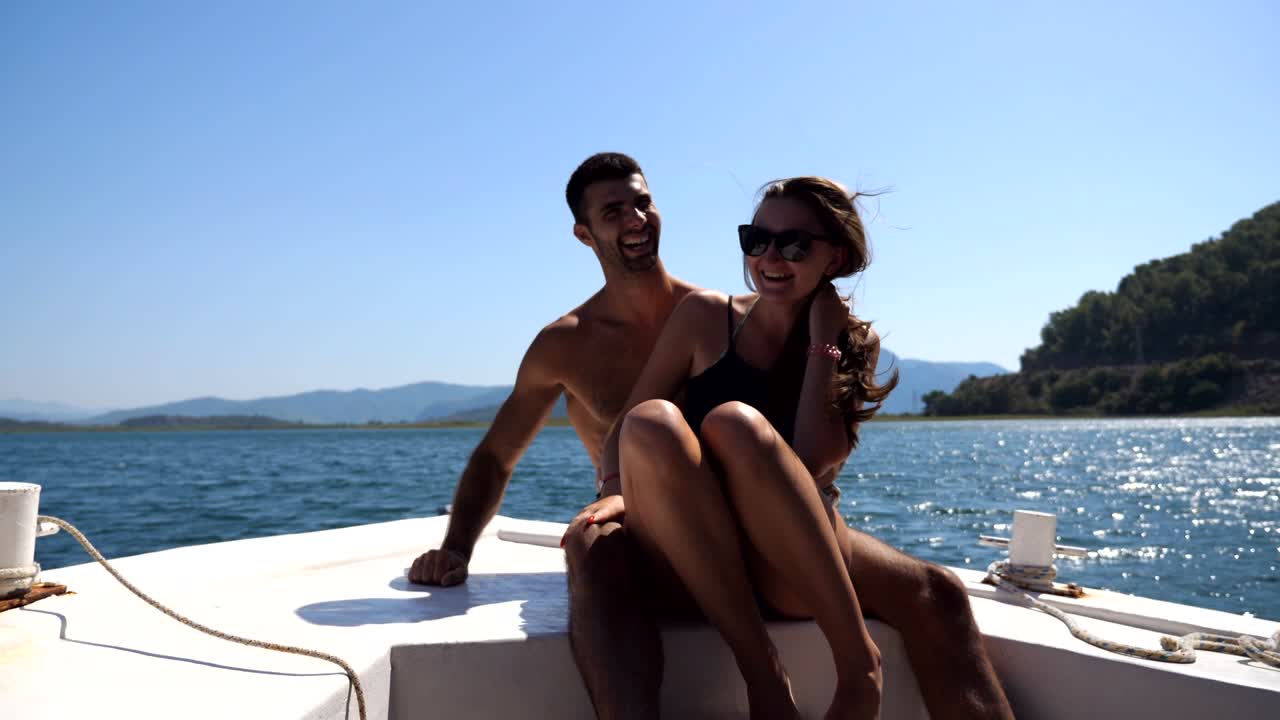 pareja joven sentada en la proa del barco y posando para el fotógrafo en un día soleado. pareja feliz enamorada pasando tiempo juntos en la cubierta del barco y disfrutando del viaje de verano. concepto de vacaciones o vacaciones. vista frontal de cerca
