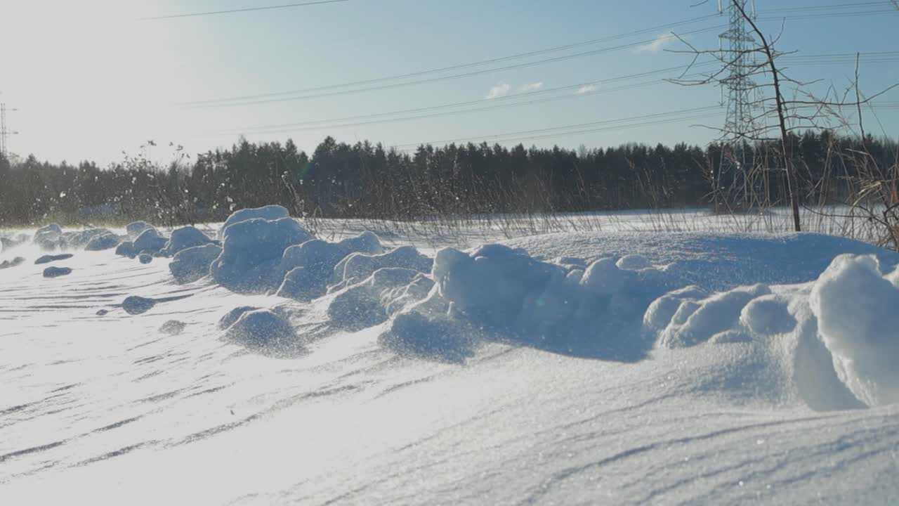 Stormy day with wind blowing loose snow around in a field in slow motion during winter time with thick snow on the ground while sun is shining. The movement of the snow is beautiful and calming.