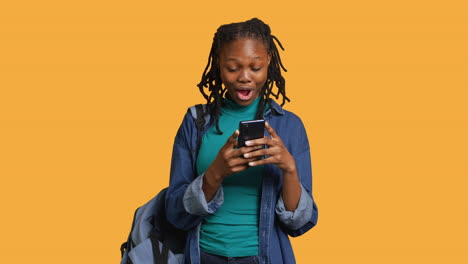 Portrait-of-overjoyed-teenager-reading-messages-on-phone,-studio-background