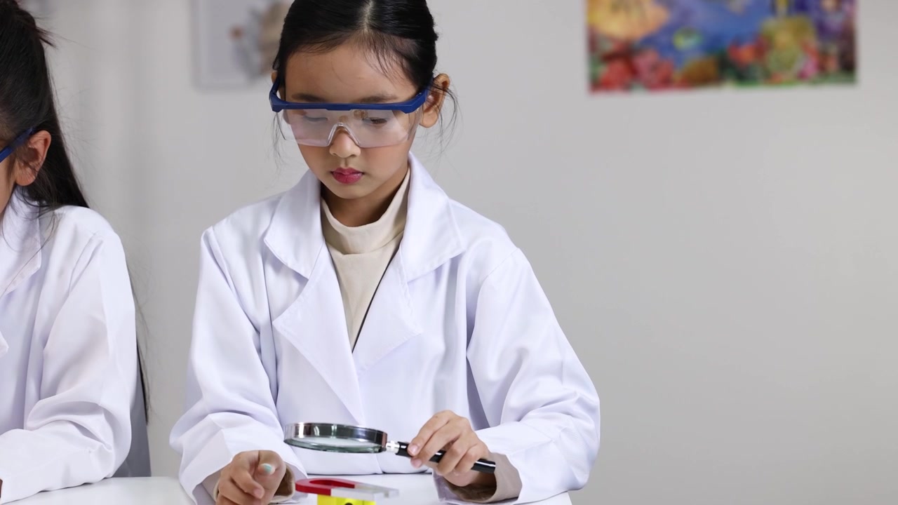 Uno studente di scuola elementare con occhiali di sicurezza esamina oggetti con una lente d'ingrandimento durante un esperimento scientifico STEM in classe.
