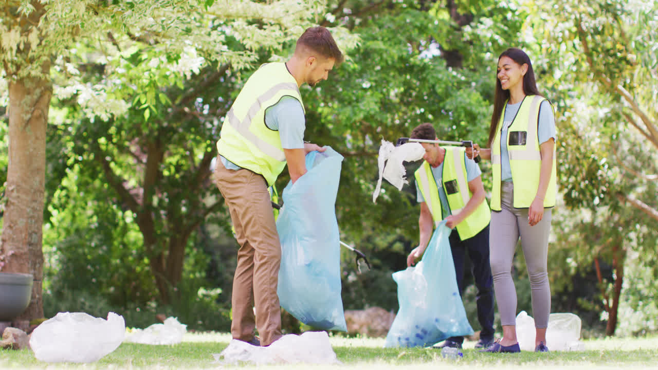 Diverse group of male and female friends putting rubbish in blue refuse sacks in forest