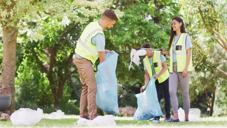 un grupo diverso de amigos masculinos y femeninos poniendo basura en bolsas de basura azules en el bosque