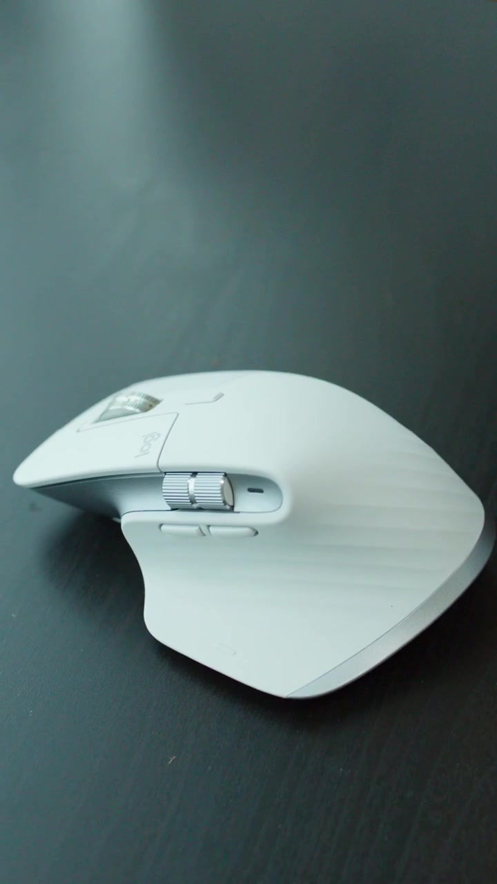 Hands unbox and place a white ergonomic mouse on a dark desk under soft daylight