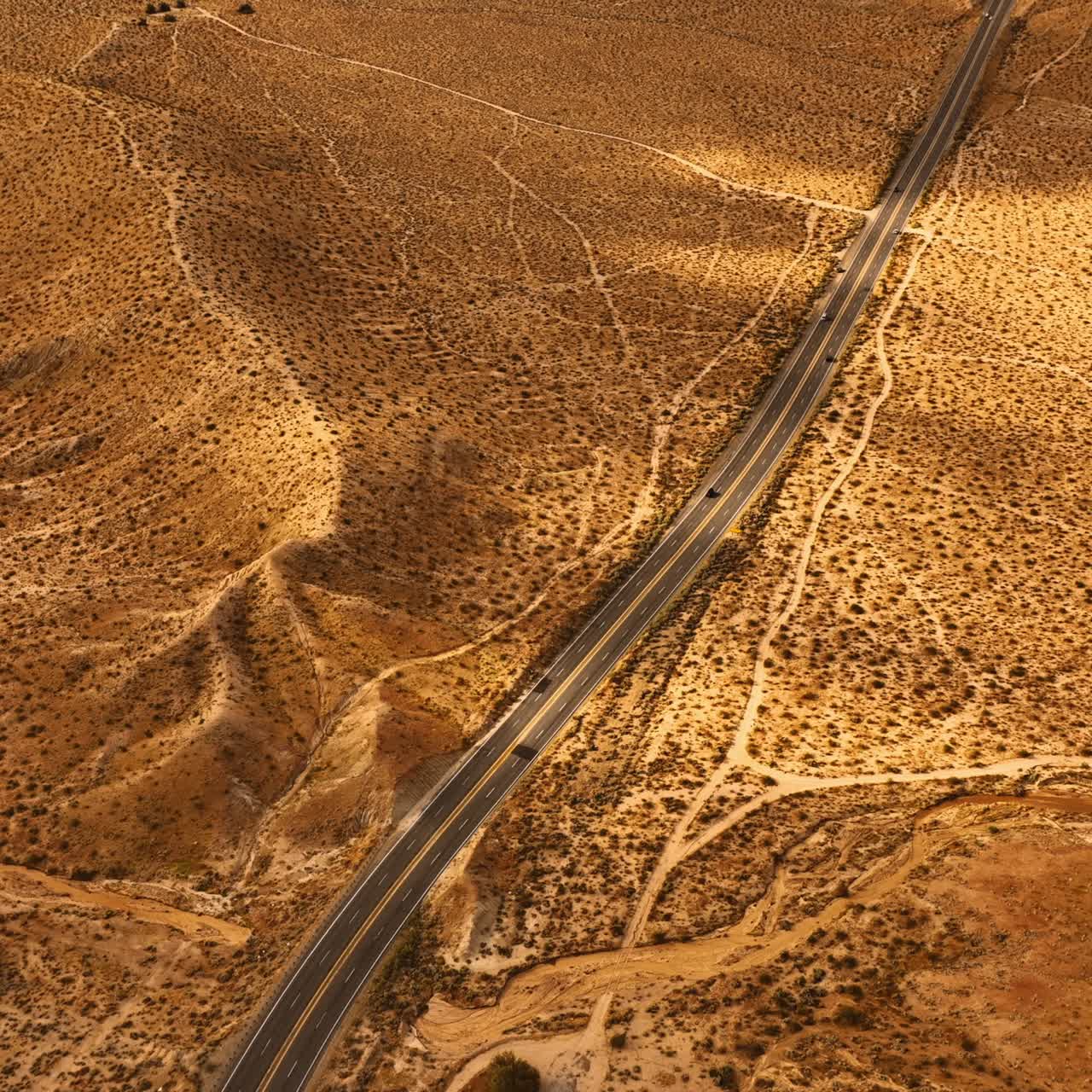 View of the highway with moving cars along the dry desert. Aerial perspective on the bare deserted landscape of Nevada