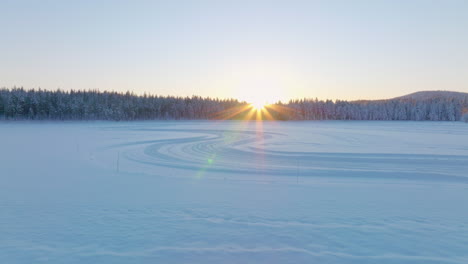 Norbotten-Swedish-Lapland-Polar-circle-ice-lake-tracks-and-woodland-aerial-view-towards-glowing-sunrise-skyline