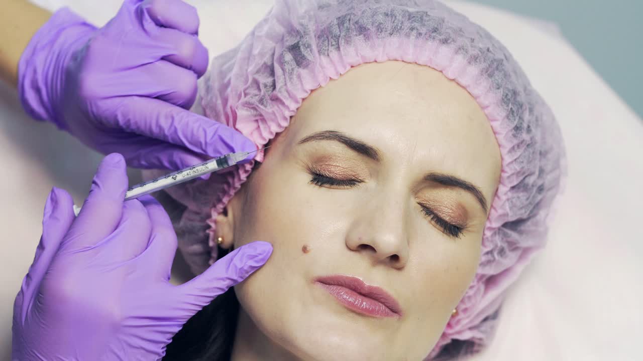 Expert beautician is filling female wrinkles by hyaluronic acid in beauty clinic. Smoothing wrinkles under eyes