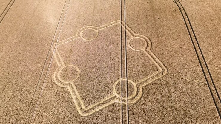 Aerial view descending towards stone henge crop circle on rural golden ploughed farmland