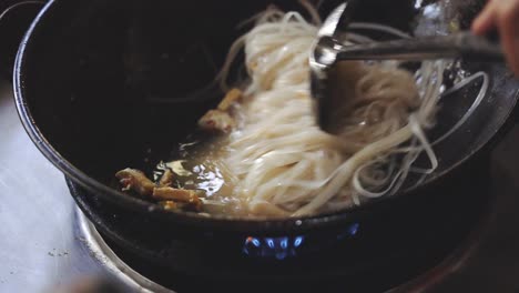 Cooking Pad Thai Series: SLO MO chef stir-frying rice noodles with Pad Thai sauce and other ingredients in hot cooking pan at Thai street food stall.