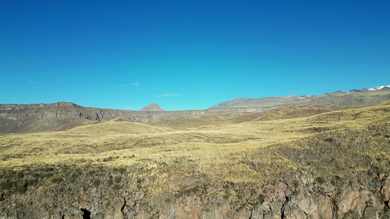 Cinematic drone reveal rising from a golden Andean valley to reveal towering snow-covered peaks glowing under morning light