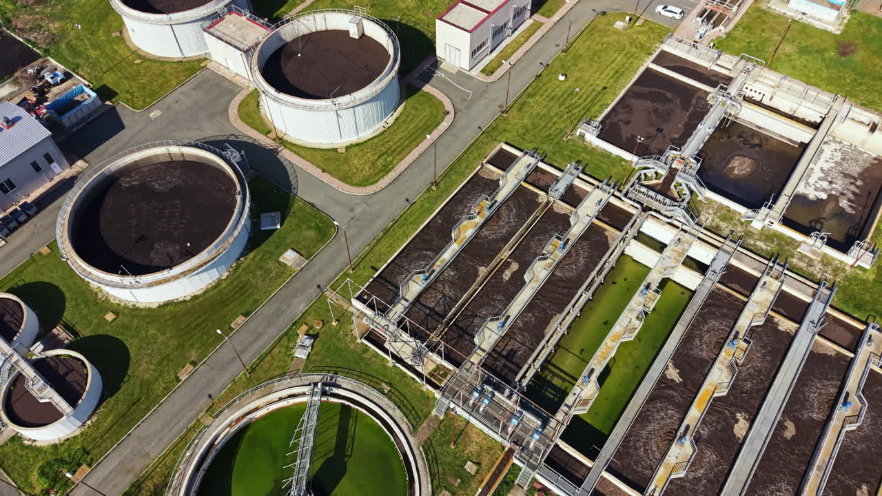 Water treatment facility shows large circular tanks and flat treatment areas under clear sky during daylight hours