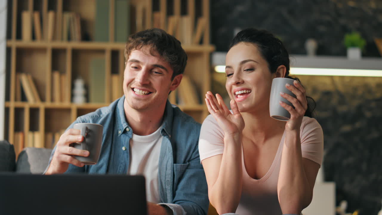 una pareja sonriente cerrando la computadora portátil terminando una reunión en línea en el sofá de casa de cerca.