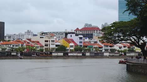 a tour boat moves slowly along the singapore river with the colourful houses that line boat quay in the background, singapore