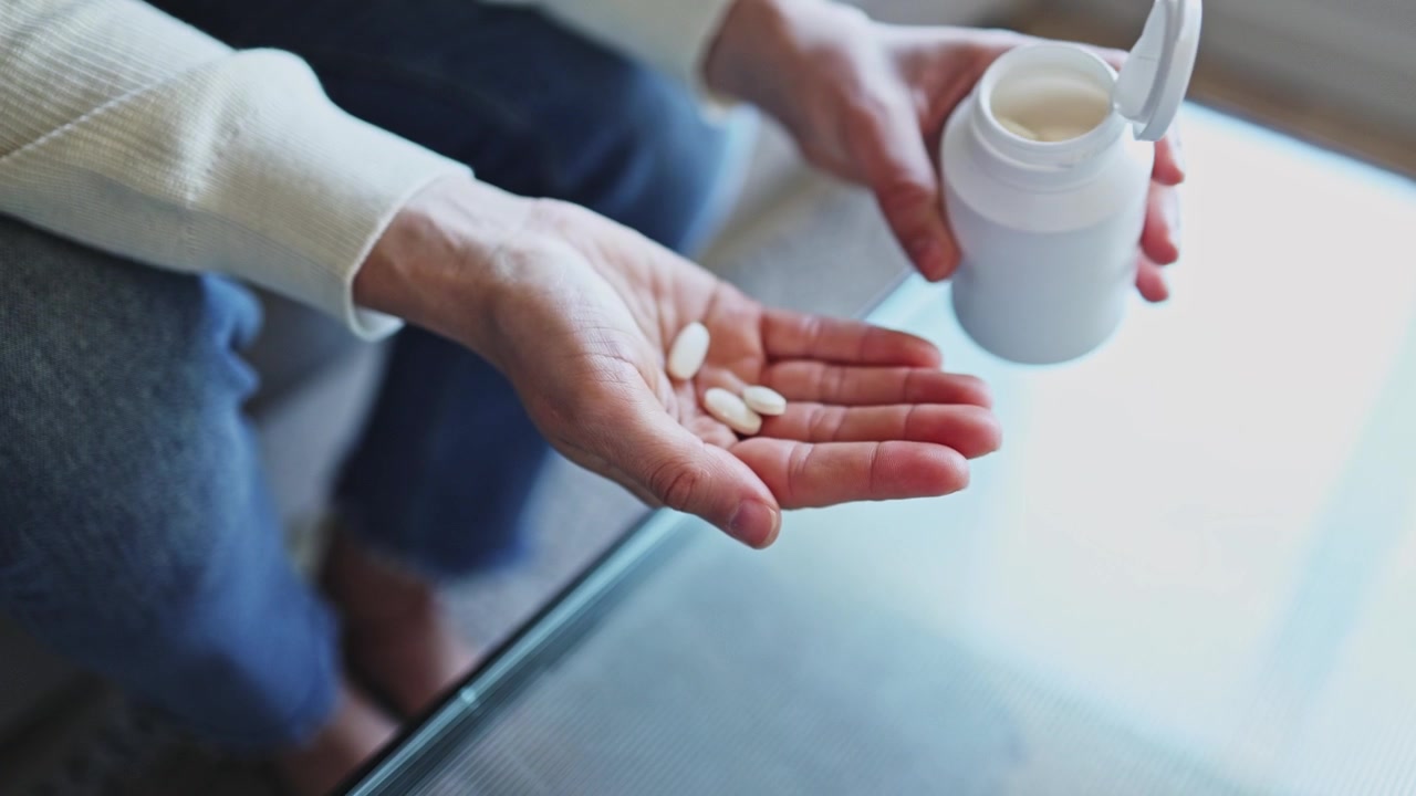 Persona vertiendo pastillas blancas de una botella en su mano